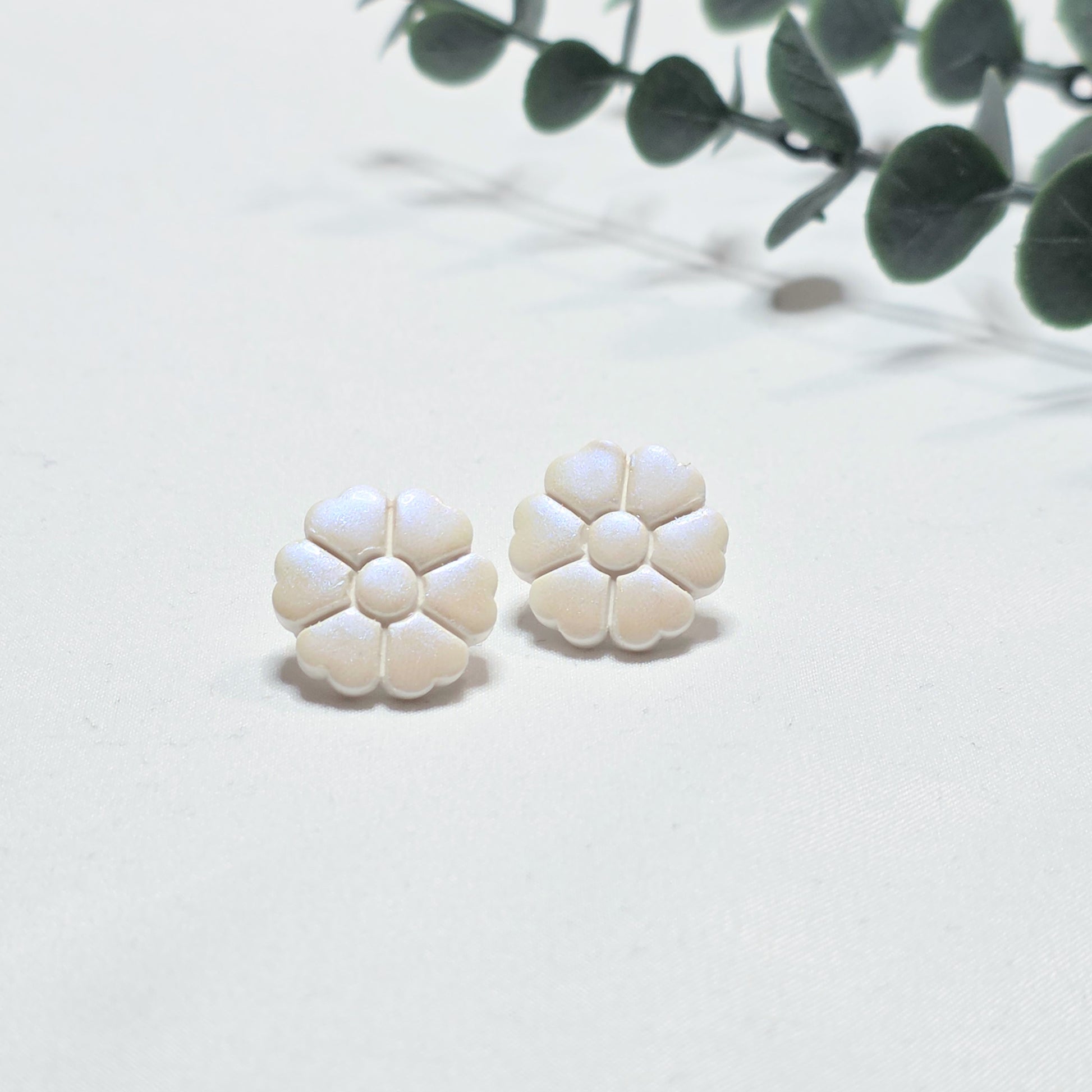 Pair of white floral earrings on a light white background with green leaves.