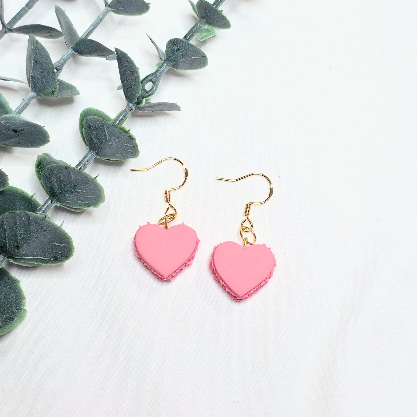 Pink heart-shaped earrings on a white background with green leaves.