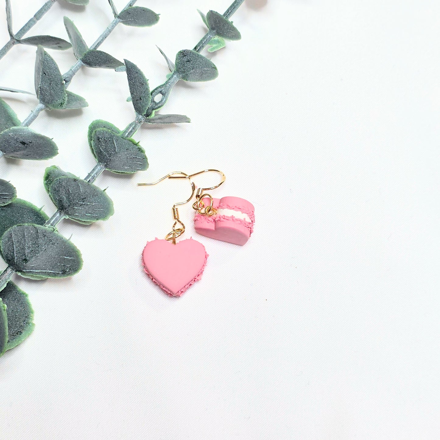 Pink heart-shaped earrings on a white background with green leaves.