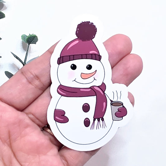 Sticker of a snowman with a purple hat and scarf held in a hand.