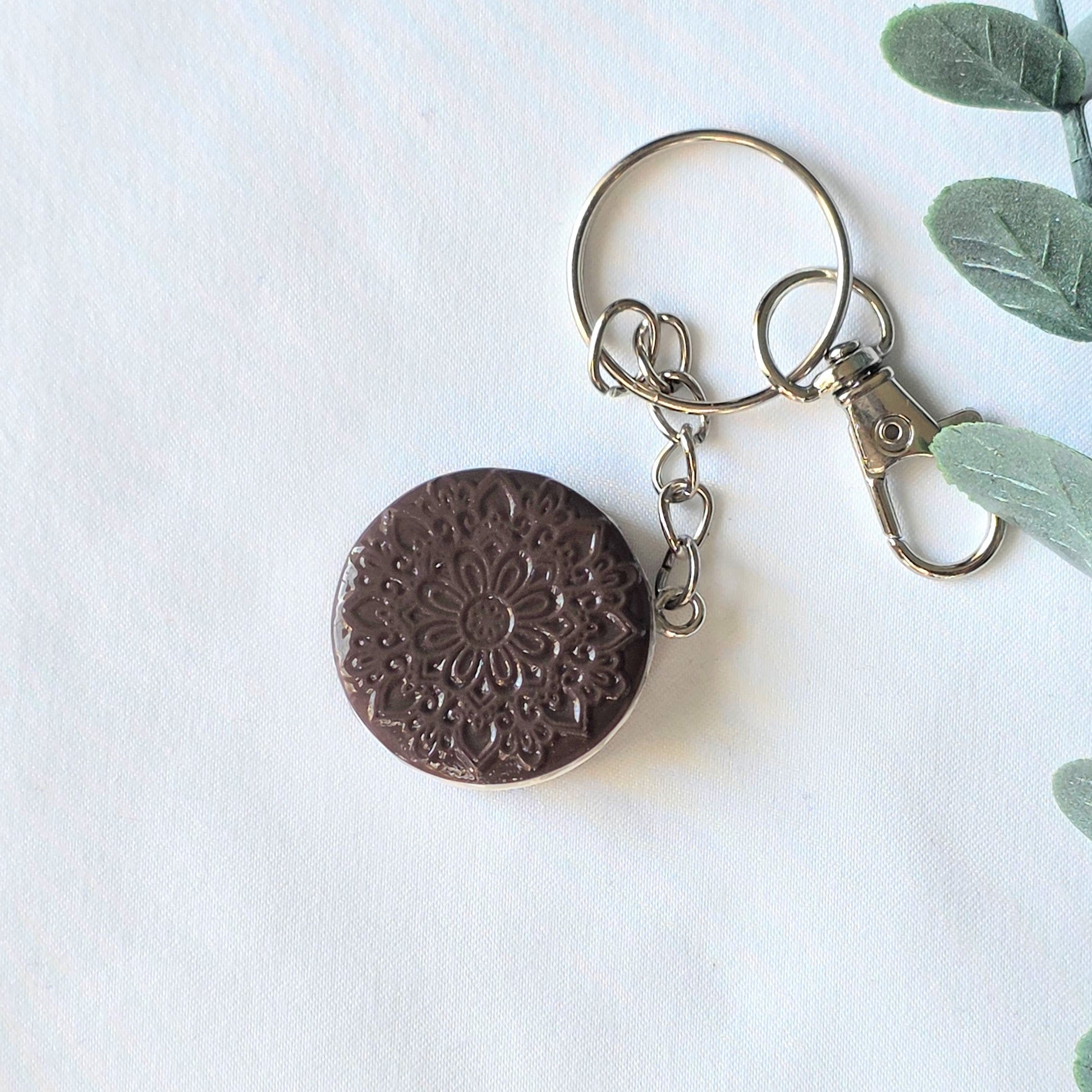 Keychain with round metal component on a white background with green leaves