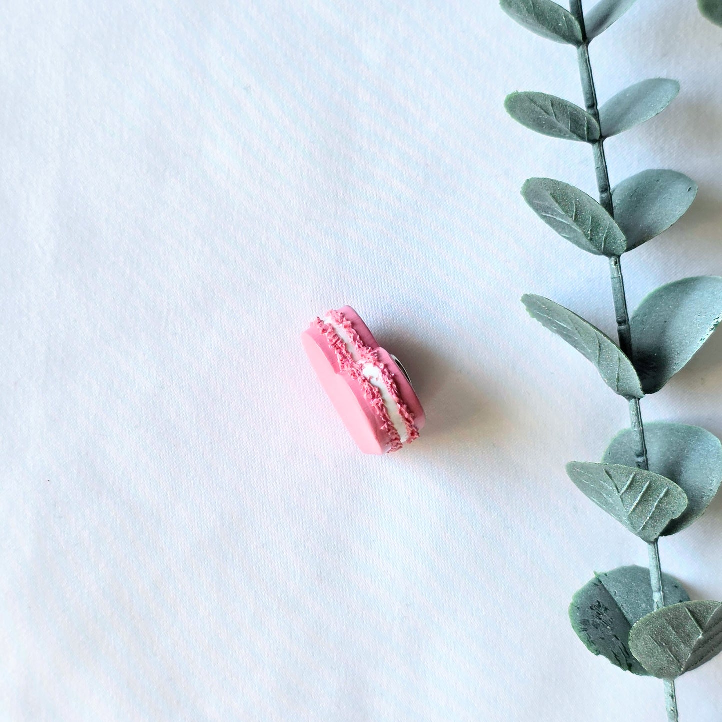 Pink macaron with white filling next to a green leafy branch on a light blue background