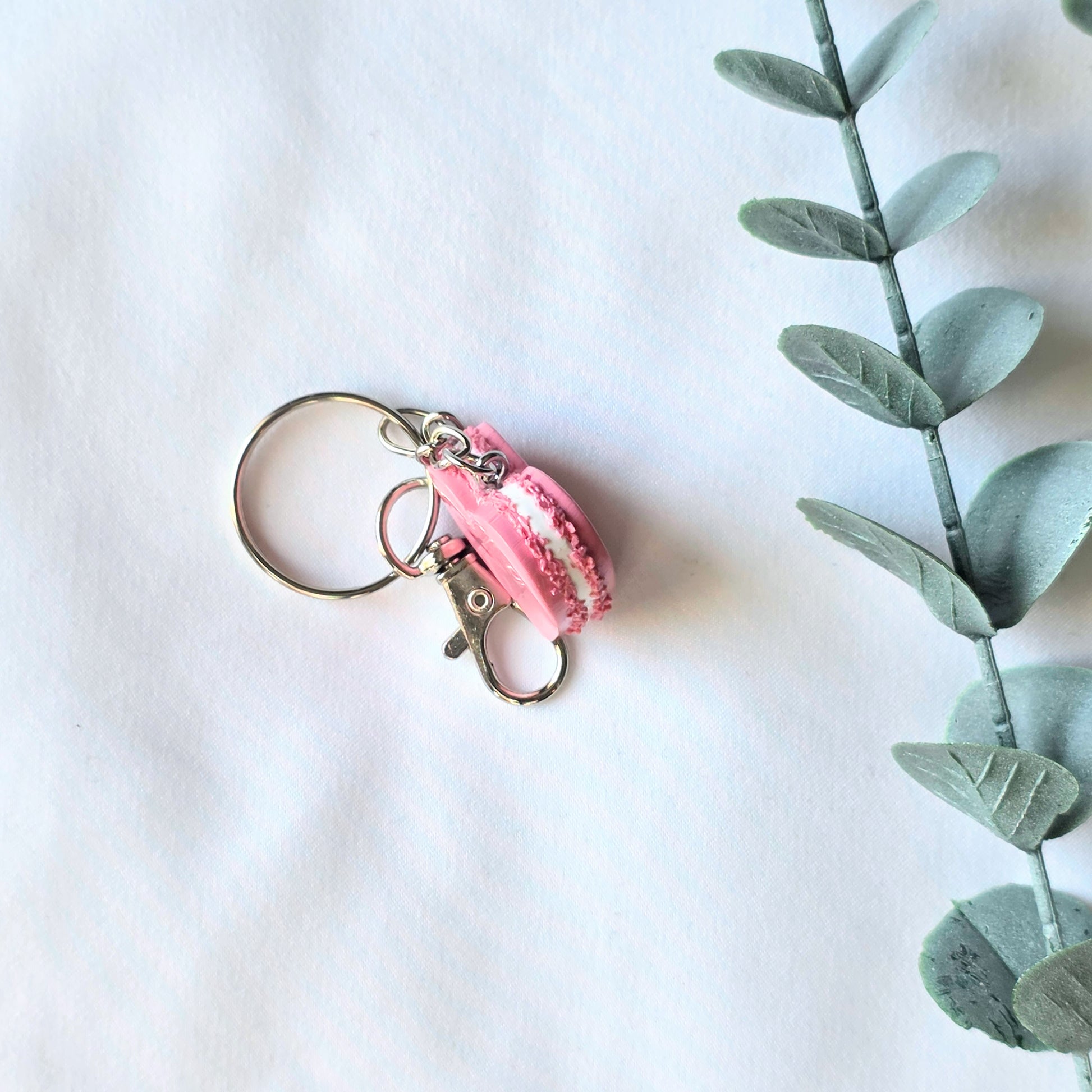 Pink macaron keychain on a white background with a sprig of eucalyptus