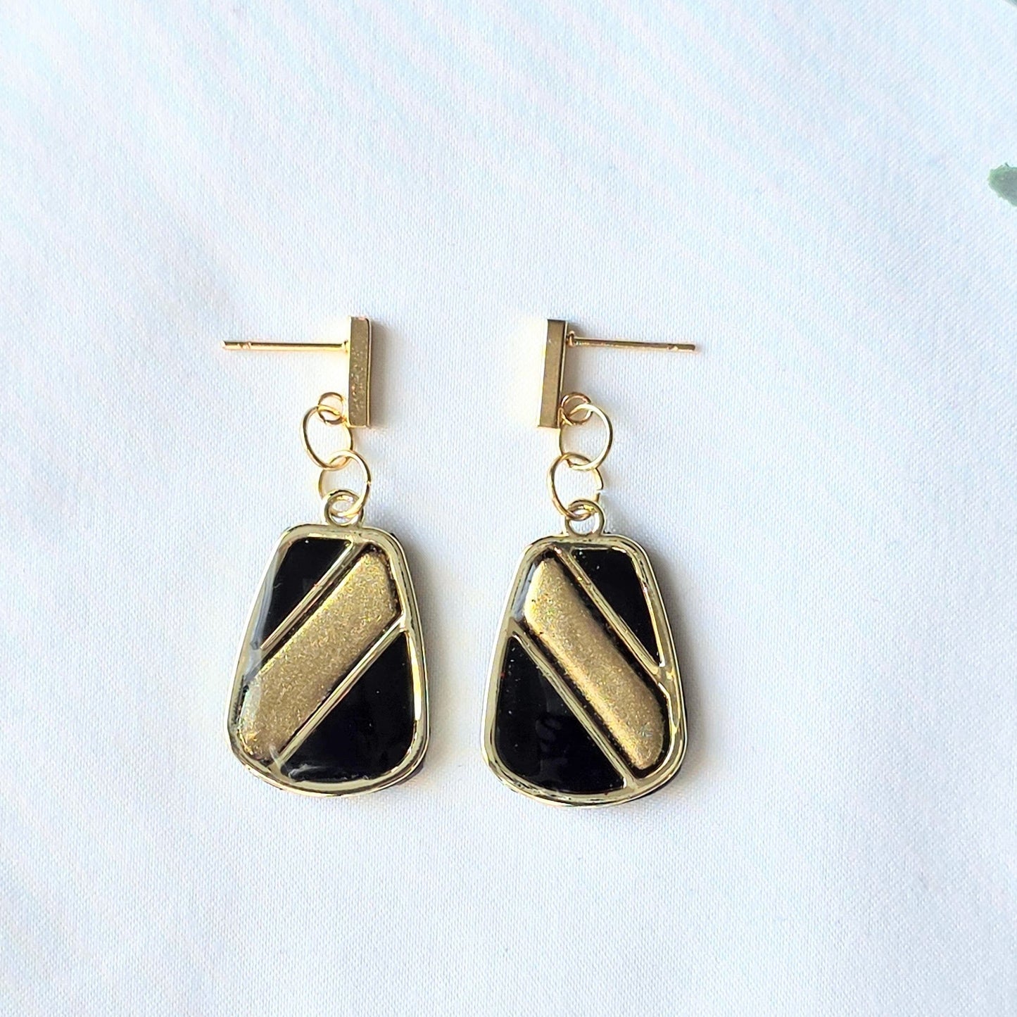 Gold and black earrings on a light gray background