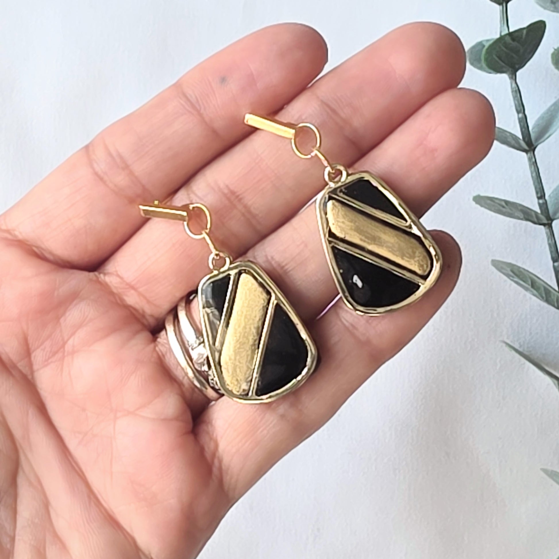 Gold and black geometric earrings held in a hand with a light background