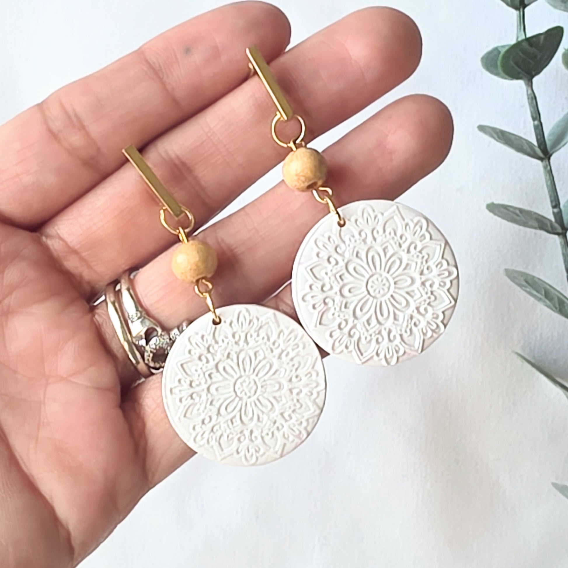 White circular earrings with gold hooks held in a hand against a white background