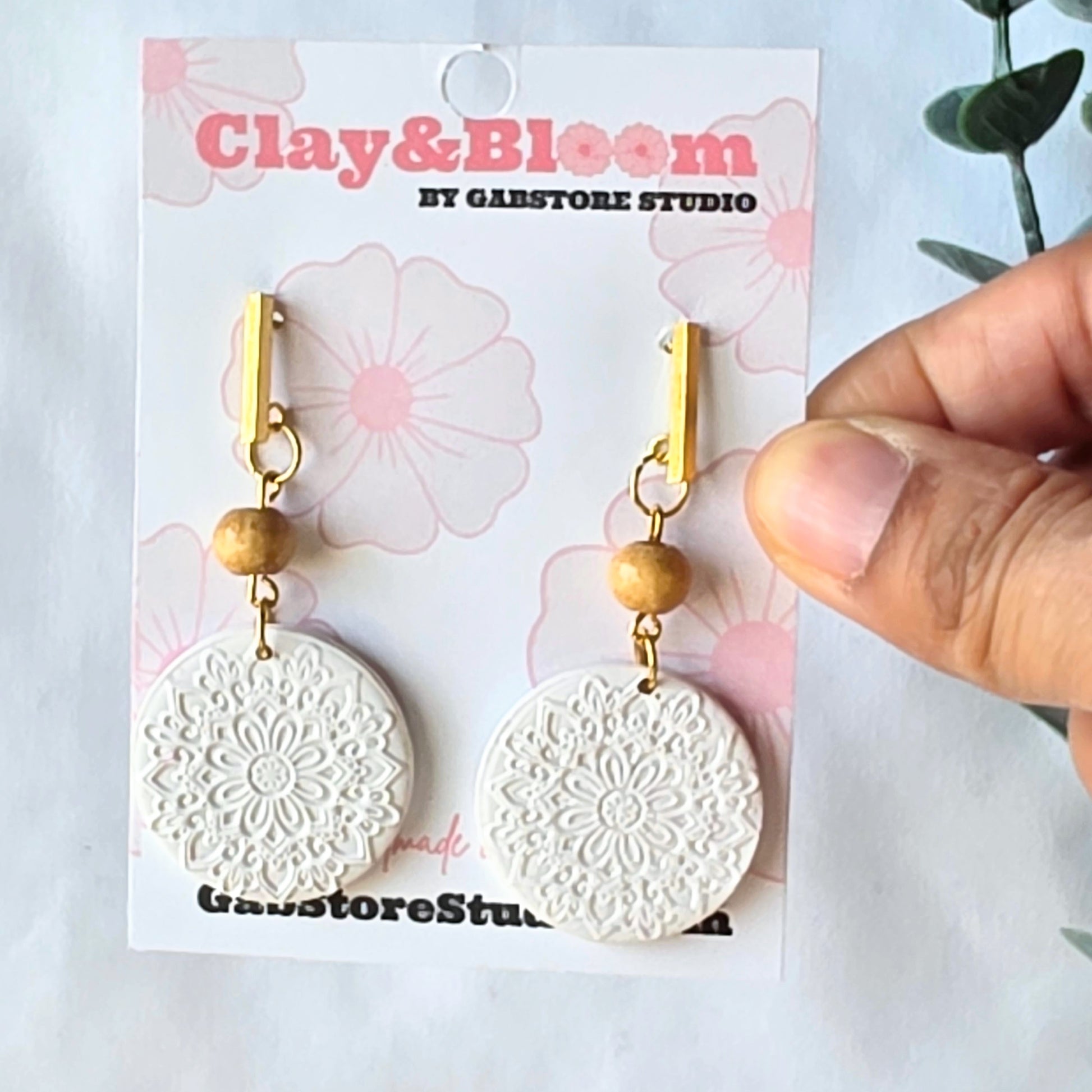 White floral-patterned earrings with gold accents on a Clay & Bloom branded card.