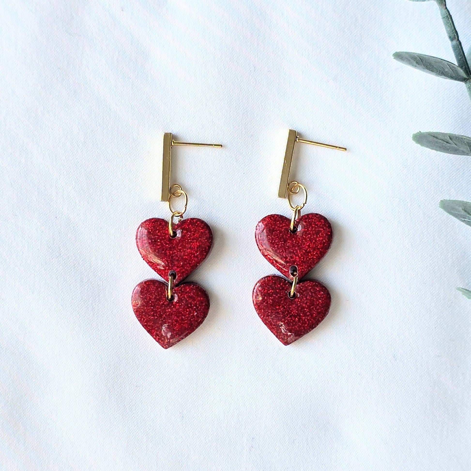 Red heart-shaped earrings on a white background with a plant leaf.