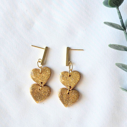 Gold heart-shaped earrings on a white background with a plant leaf.