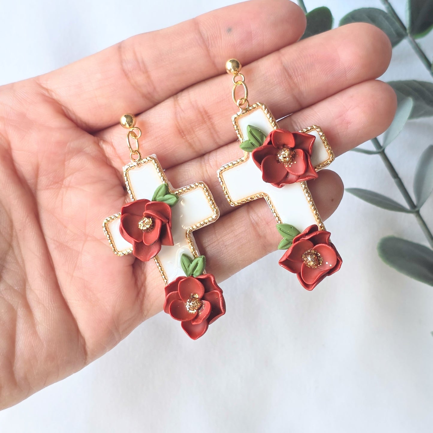 Earrings with red floral designs held in a hand against a white background