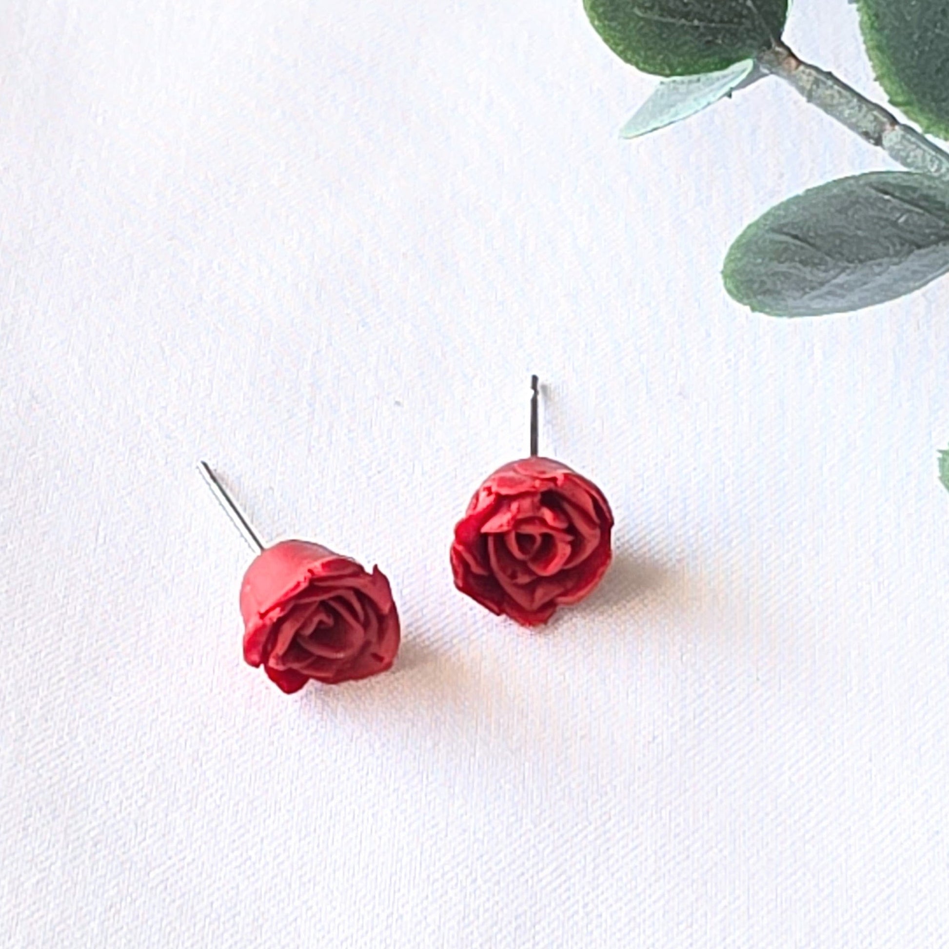 Red rose earrings on a white background with green leaves.