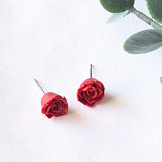 Red rose earrings on a white background with green leaves.