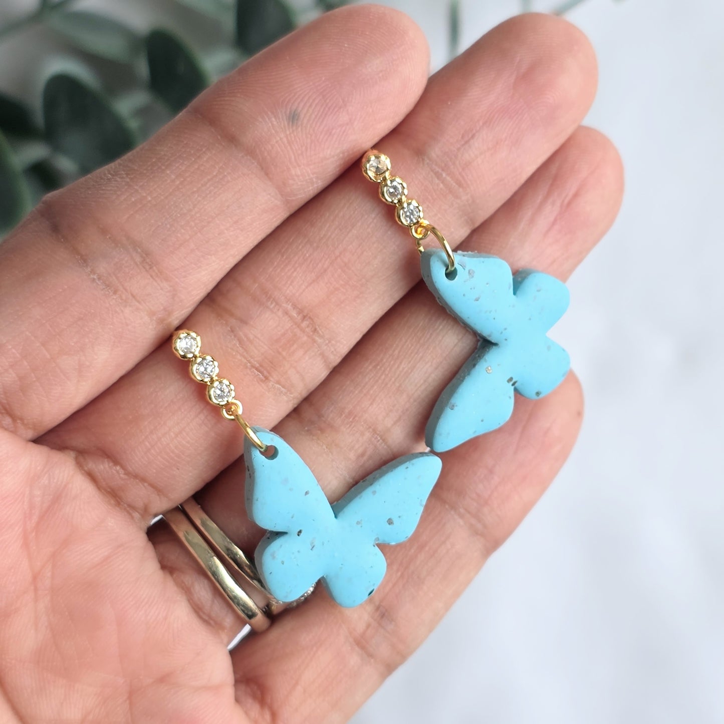 Blue butterfly earrings held in a hand with a blurred background