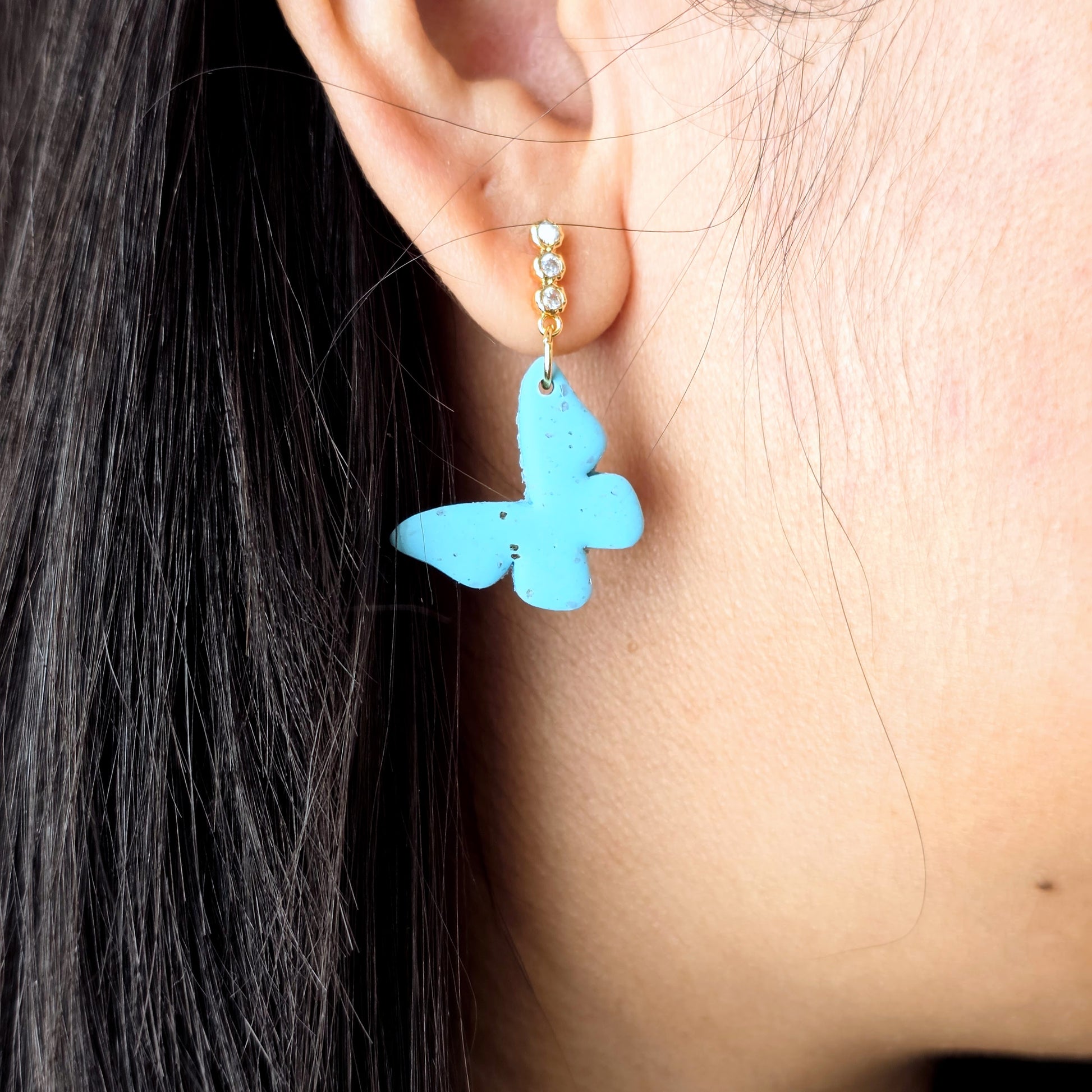 Close-up of a turquoise butterfly earring on an ear.