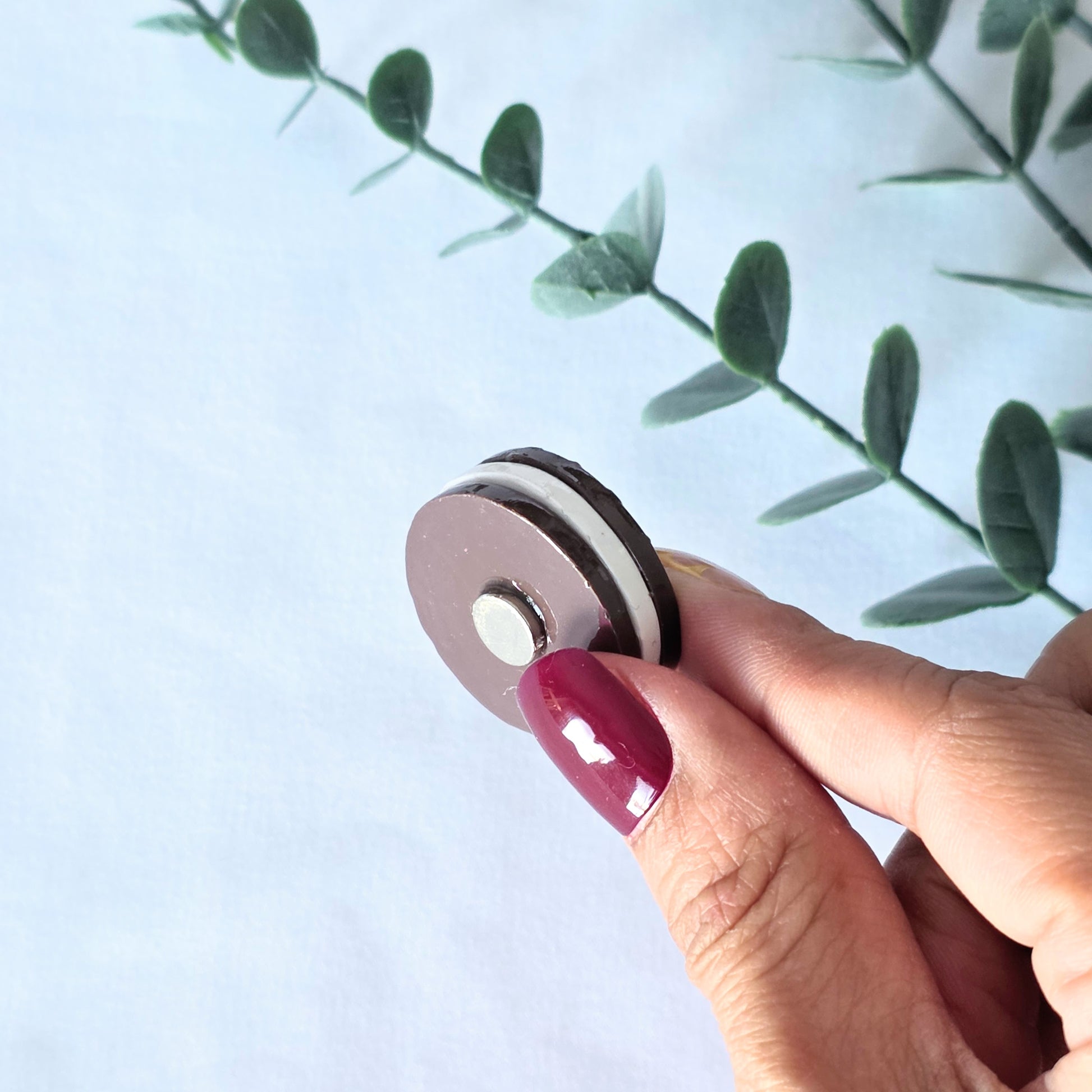 Hand holding a polymer clay cookie magnet against a white background with green leaves.