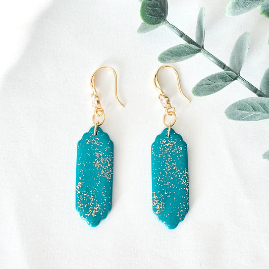 Teal earrings with gold speckles on a white background with green leaves.