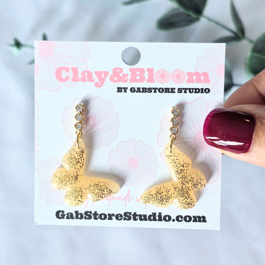 Gold glittery earrings on a Clay&Bloom branded card with a blurred background
