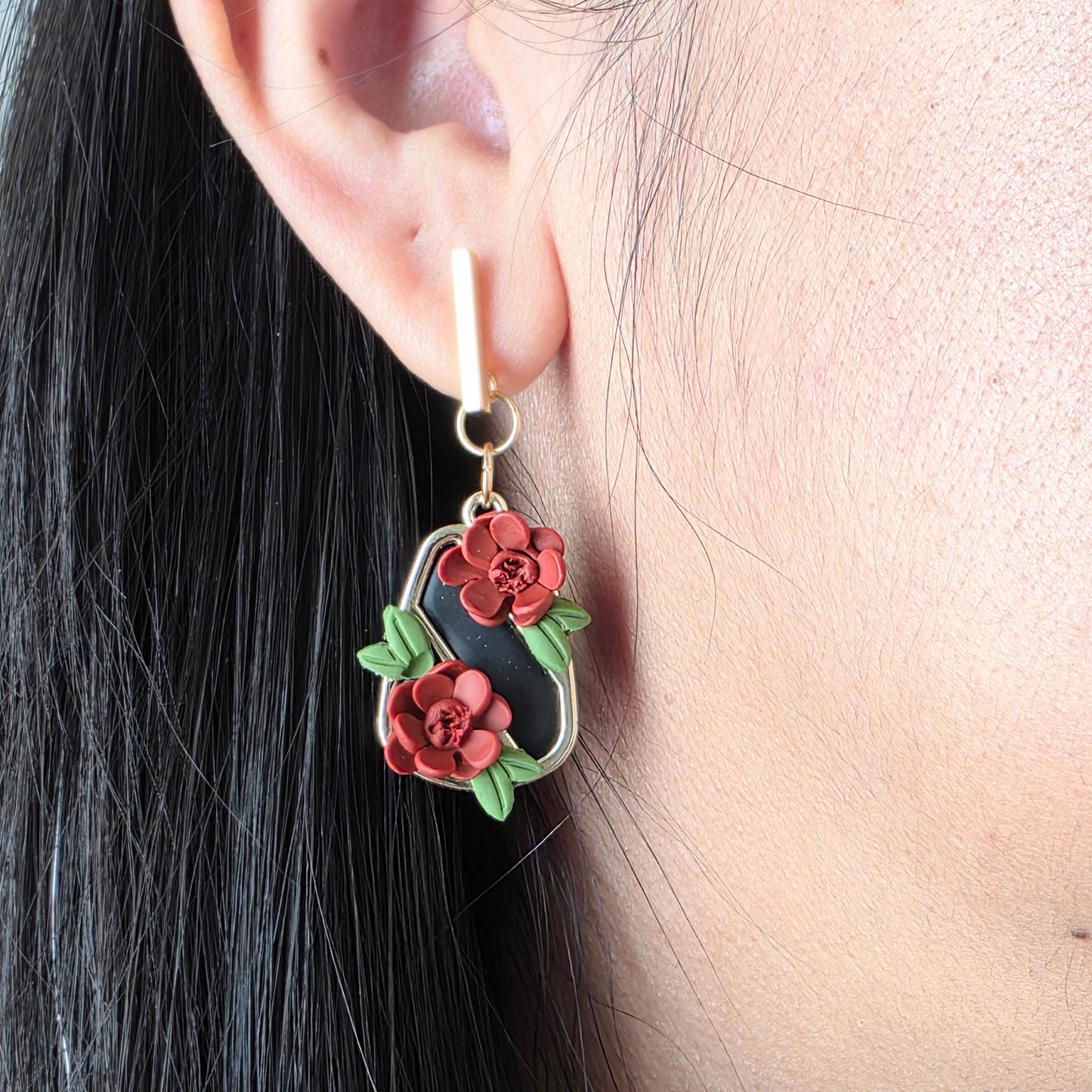Floral earrings worn by a person with dark hair.