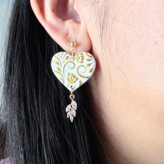 Heart-shaped earrings with gold patterns worn by a person with black hair.