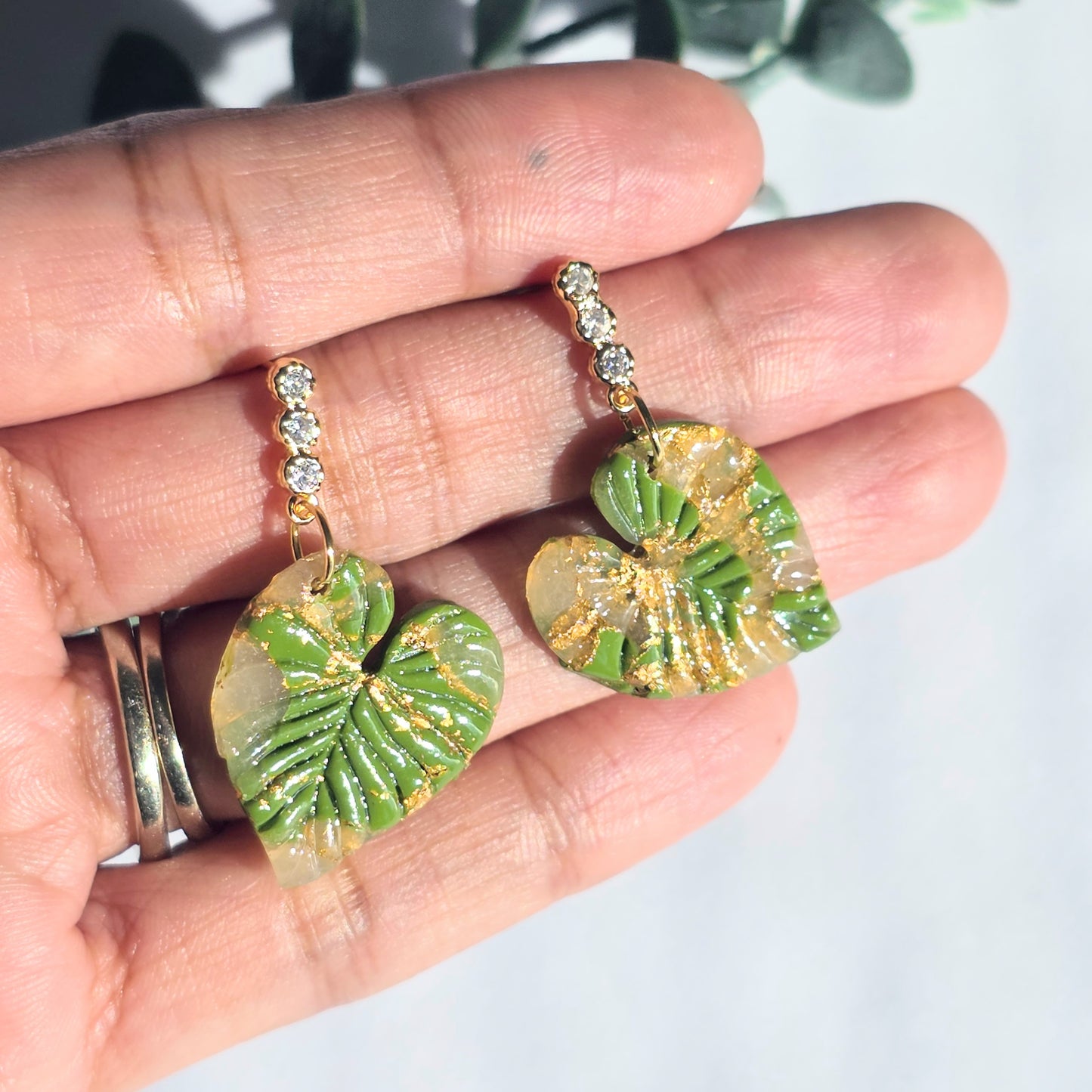 Green leaf-shaped earrings held in a hand with a light background