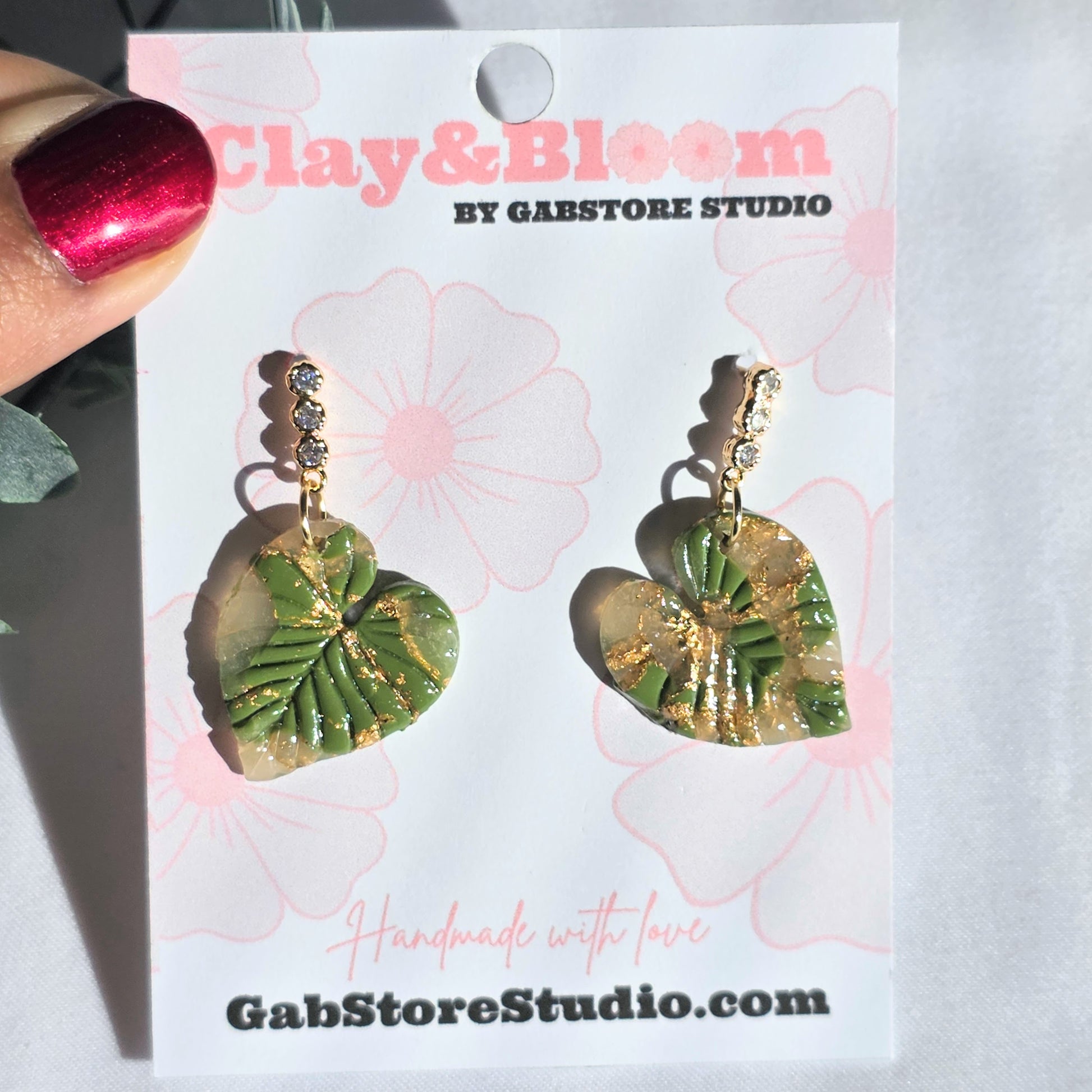 Green leaf-shaped earrings on a 'Clay & Bloom' branded card.