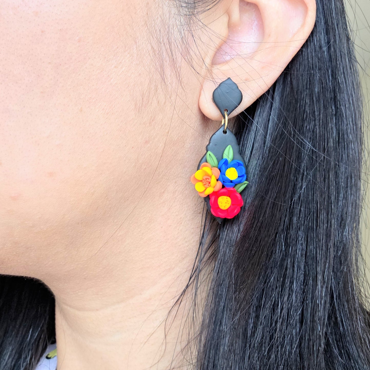 Earring with colorful floral design worn by a person with dark hair.