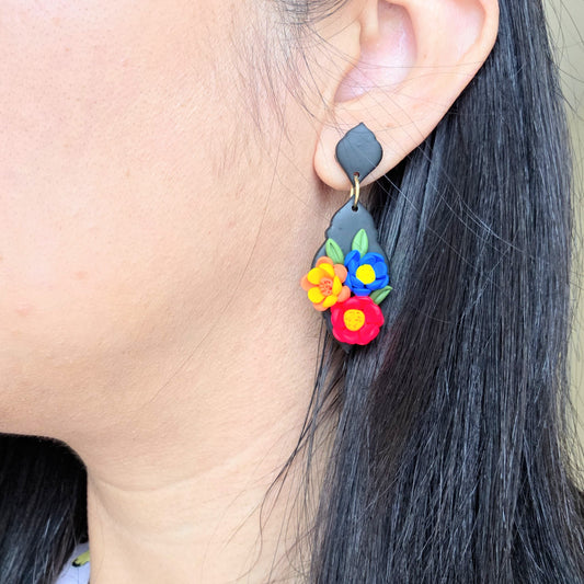 Earring with colorful floral design worn by a person with dark hair.