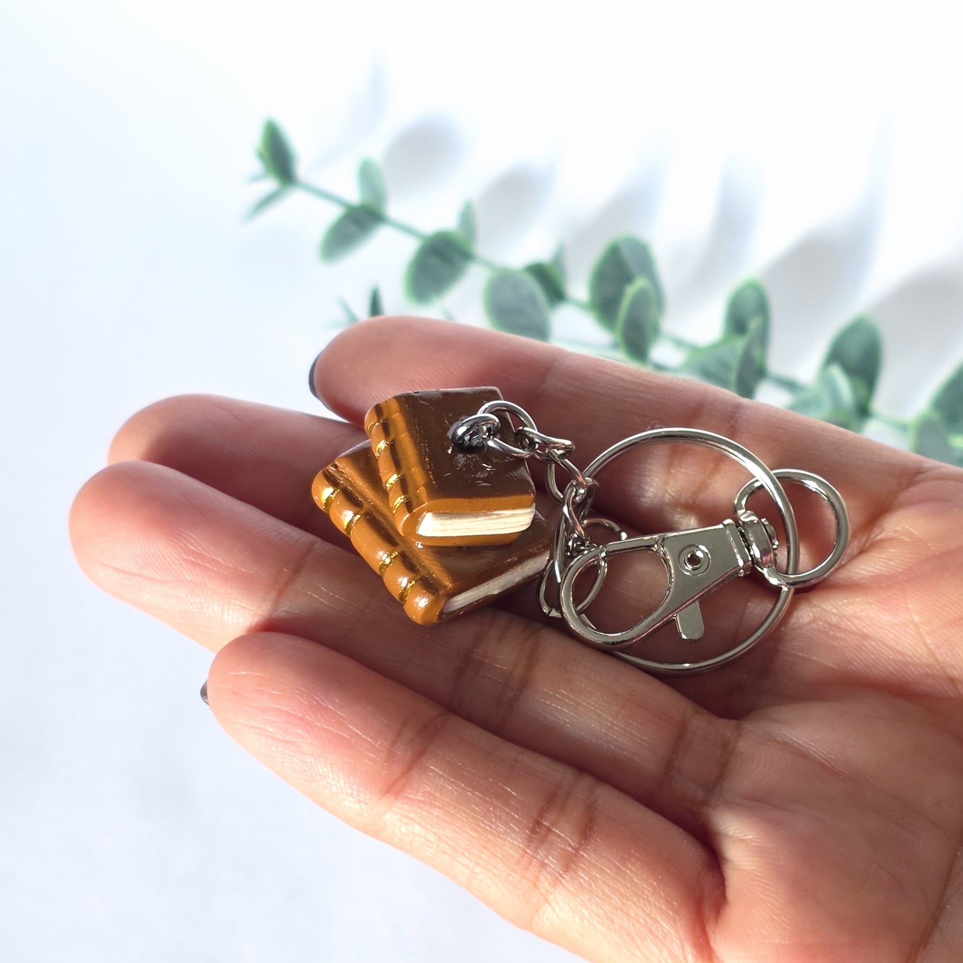 Hand holding a keychain with a book-shaped charm against a blurred natural background