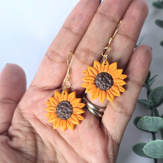 Sunflower-shaped earrings held in a hand with a light background