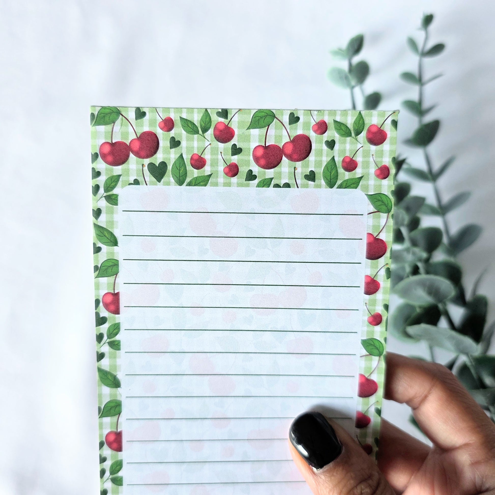Notepad with cherry design held by a hand against a white background