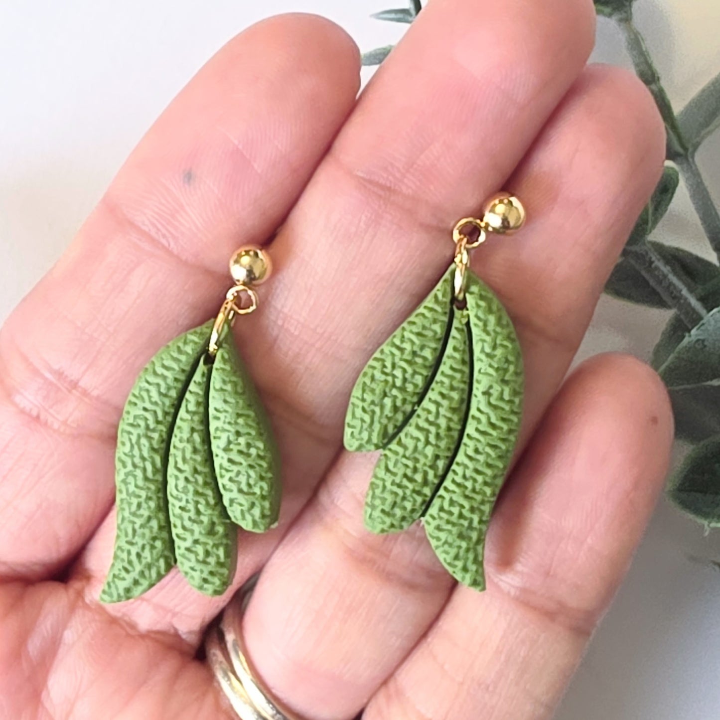 Green leaf-shaped earrings with gold hooks held in a hand.