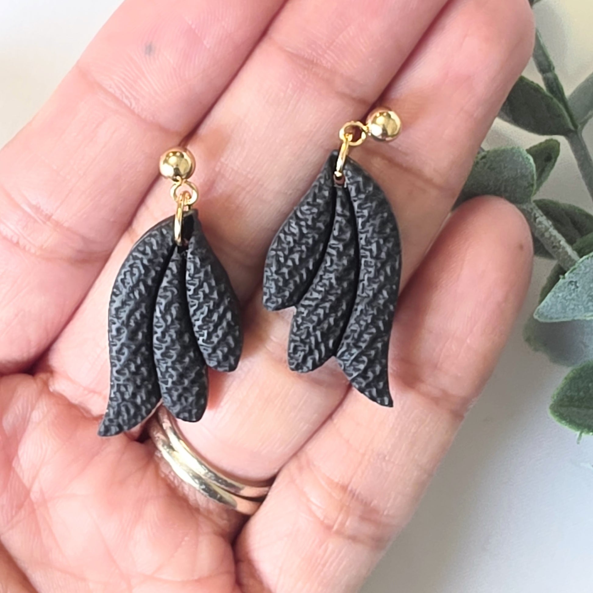 Black feather-shaped earrings with gold hooks held in a hand.