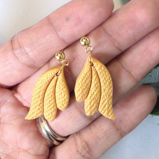 Gold leaf-shaped earrings held in a hand.