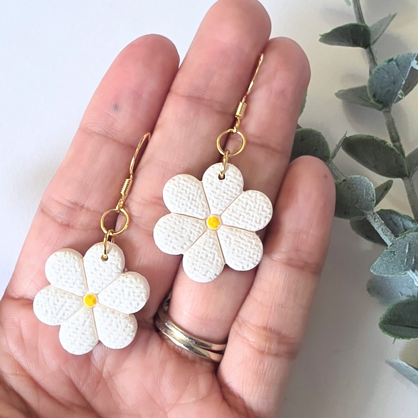 White flower earrings with gold hooks held in a hand against a light background.