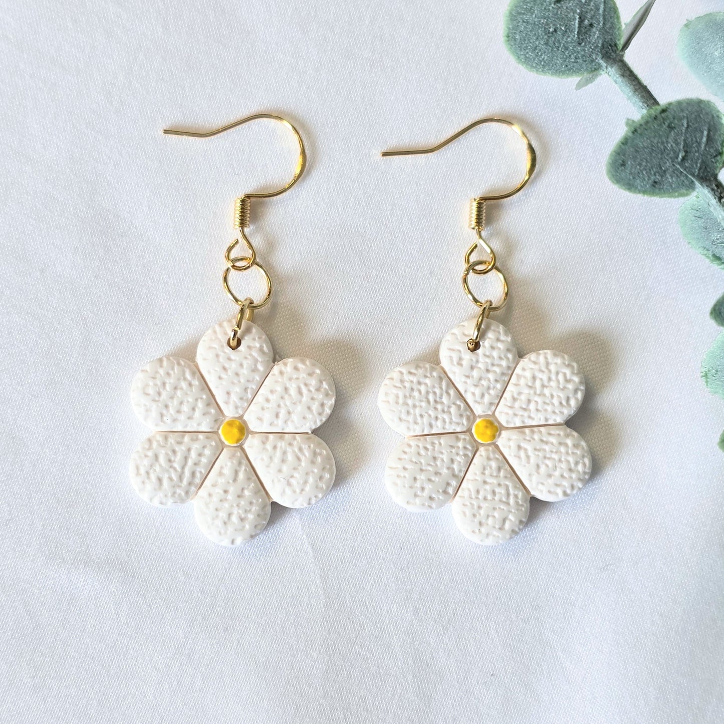 White flower-shaped earrings with gold hooks on a light gray background