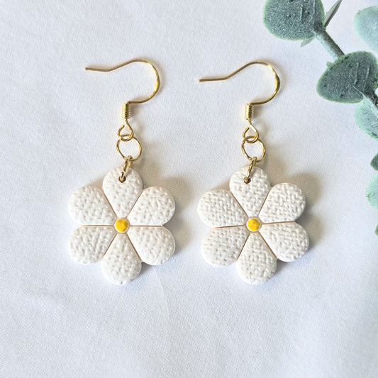 White flower-shaped earrings with gold hooks on a light gray background